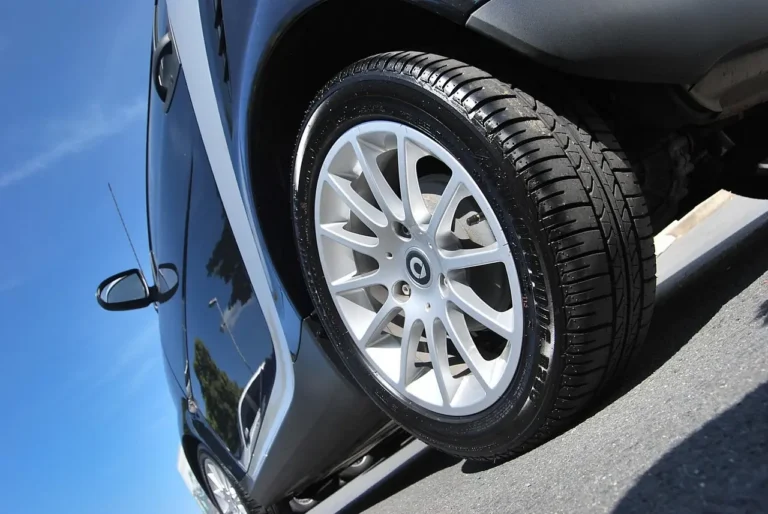 Car detailer scrubbing a dirty tire with foam cleaner beside a parked vehicle