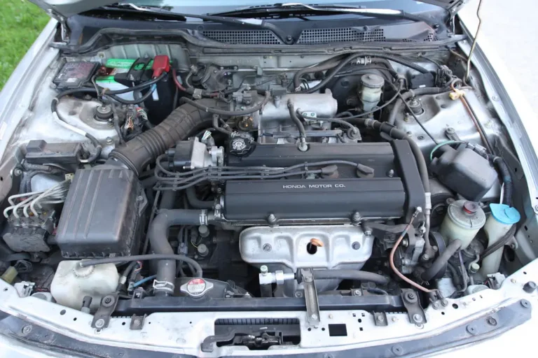 Mechanic comparing a cooling system flush kit beside an open car hood in a garage