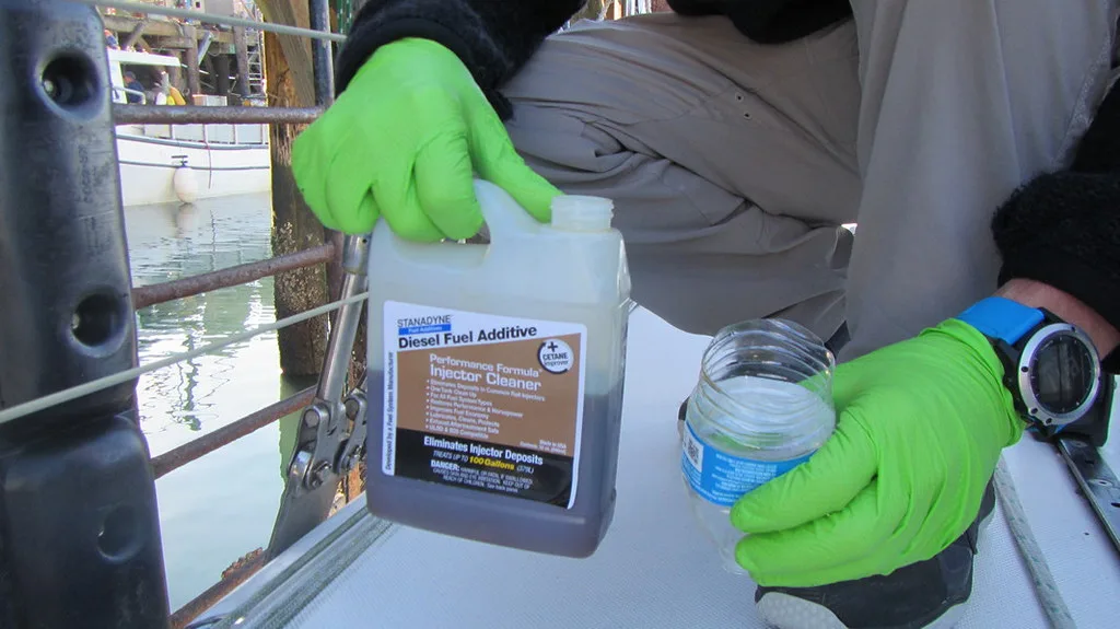 Hand pouring fuel injector cleaner into a measuring cap beside an open engine bay