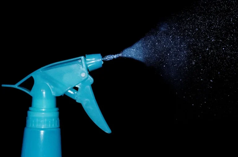 A person arranges hoses and nozzles beside an SUV in a driveway, ready for car washing.