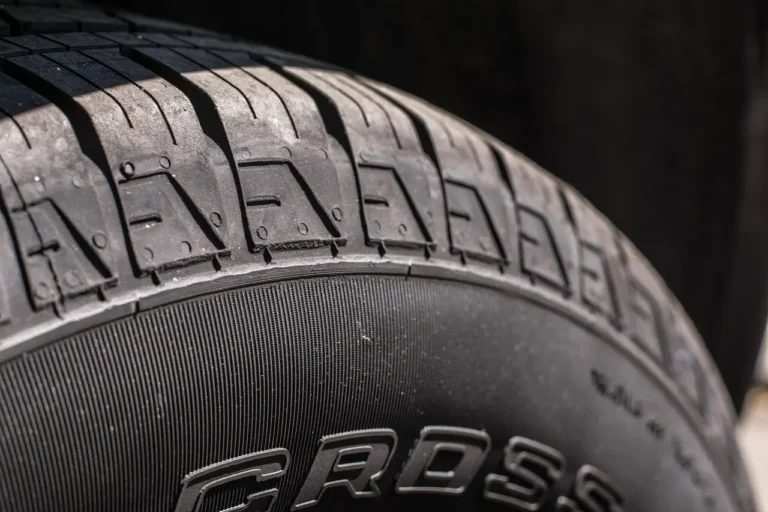 Three car tires beside a sedan on a driveway in natural morning light.