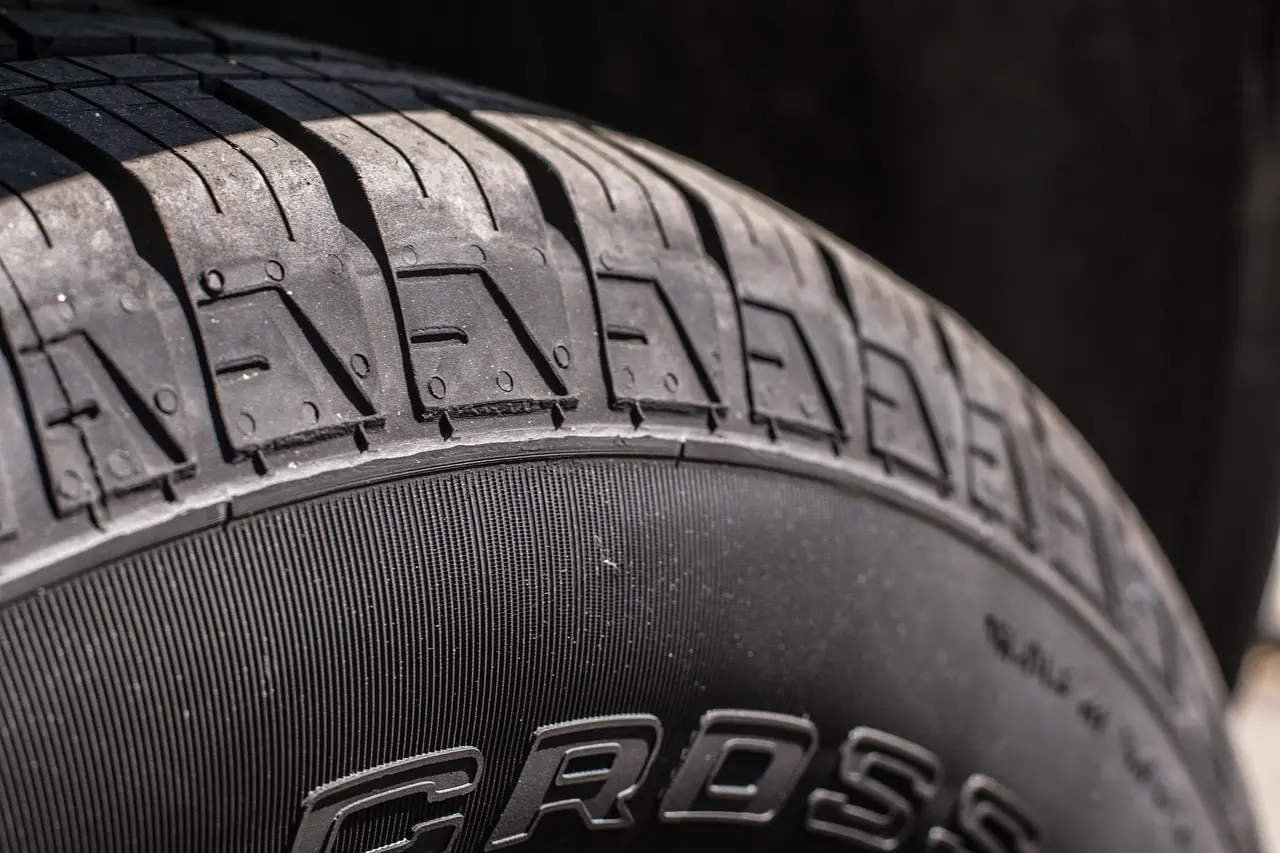 Three car tires beside a sedan on a driveway in natural morning light.