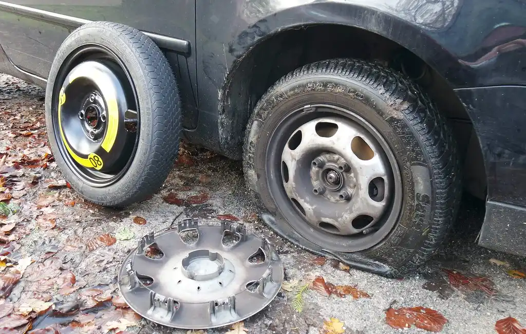 Hands using a tread gauge on a car tire in a garage.
