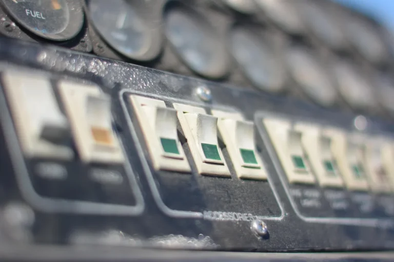 Three car battery switch disconnect options beside a battery on a garage workbench