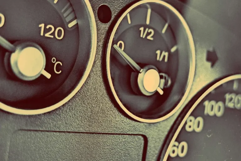 Three outside temperature gauges for a car beside a sedan, with sensor probes and display units on a workbench