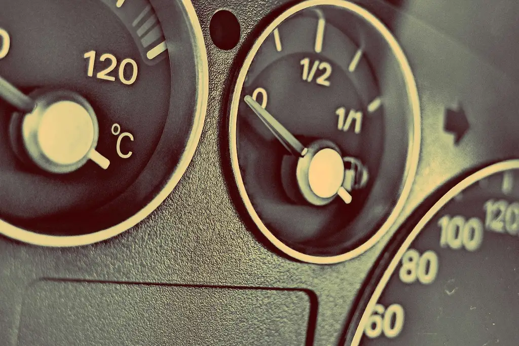 Three outside temperature gauges for a car beside a sedan, with sensor probes and display units on a workbench