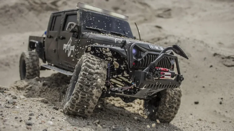 RC truck with paddle tires driving across wet beach sand near the shoreline