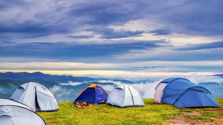Camping privacy tent beside a small SUV with a hanging portable shower bag and separated wet gear