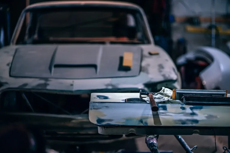 Three primer paint cans beside a car panel with rust, sanding marks, and a plastic bumper sample