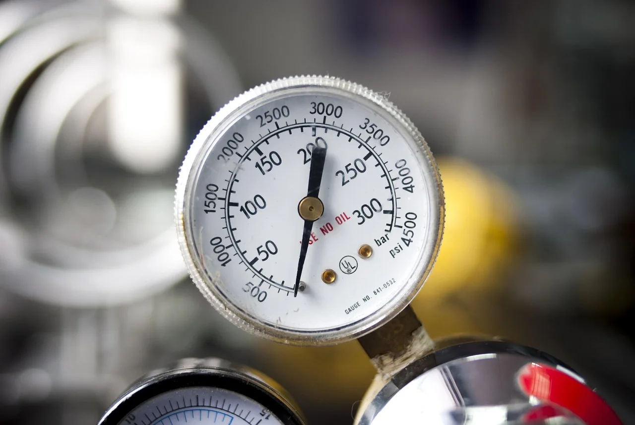 Driver comparing a digital and pencil PSI gauge beside an open car trunk