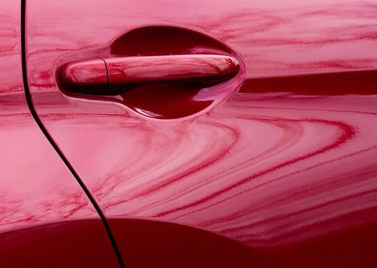 Three red car paint options on a garage workbench beside a masked panel and swatches