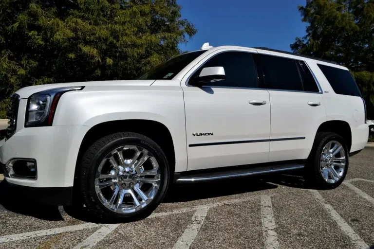 Midsize SUV beside four all-season tires on a driveway with a mechanic checking tread depth