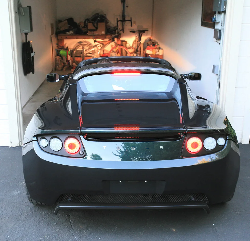 EV charging plug connected to a home wall charger beside a luxury electric sedan