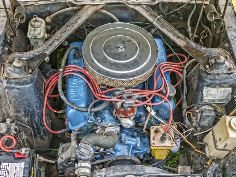 Mechanic checks a car alternator and battery under an open hood with a multimeter