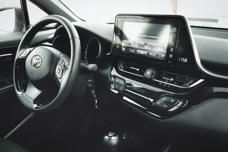 Car floor mats laid out beside an open sedan as a person compares fit and material