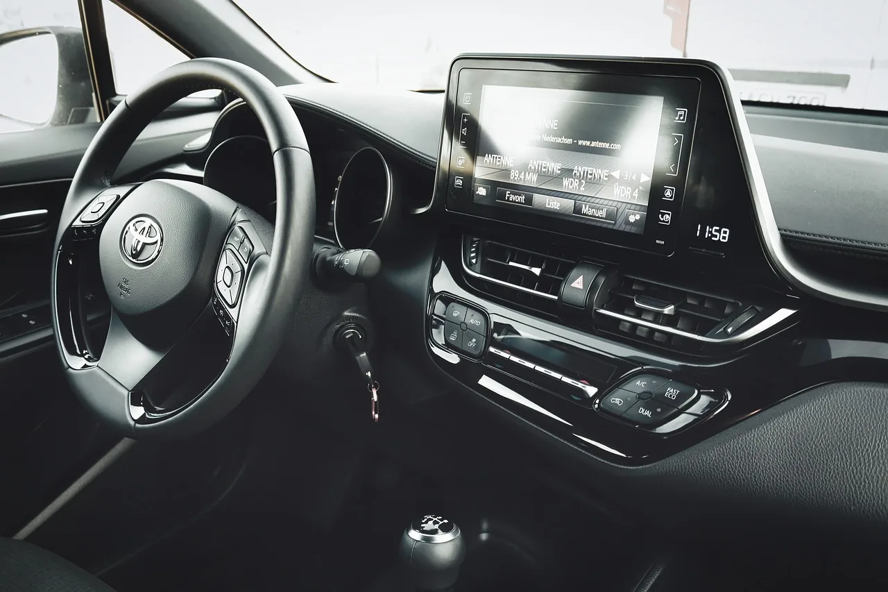 Car floor mats laid out beside an open sedan as a person compares fit and material