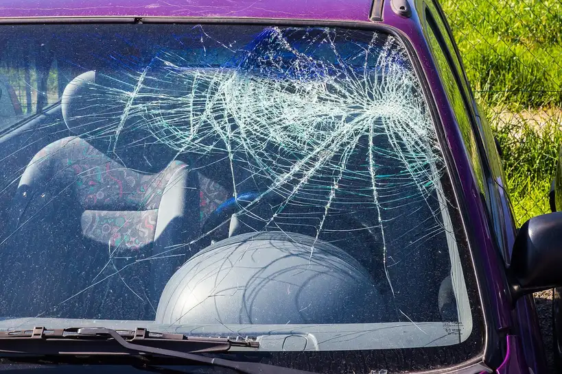 Car owner inspecting a cracked windshield on a parked sedan in natural daylight