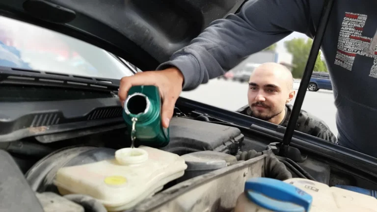 Busy professional checks tire pressure beside a modern sedan in a sunlit driveway.