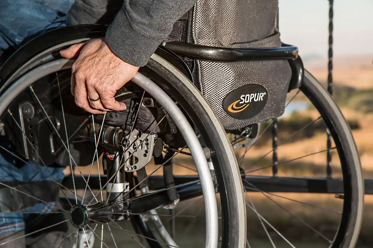 Person measuring a wheelchair beside a hitch car carrier in a driveway