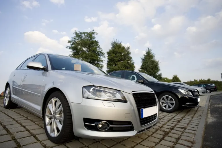 Shoppers comparing new cars on a U.S. dealership lot while a salesperson stands nearby.