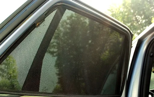 Driver comparing three car sun shades fitted across a sedan windshield in natural daylight