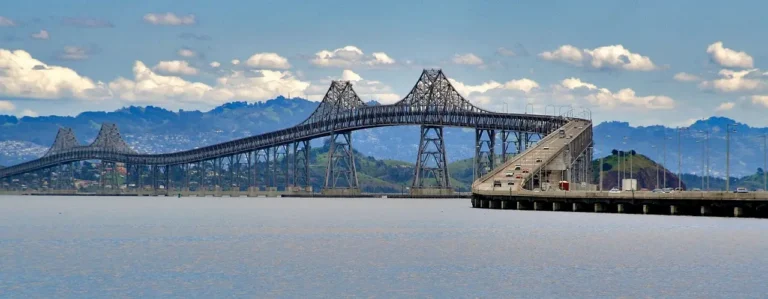 The Bay Bridge spans calm water at sunrise with a small emergency boat below.