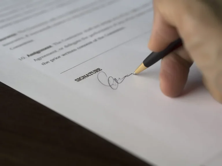 A car buyer reviews auto loan paperwork on a kitchen table beside a laptop and smartphone.