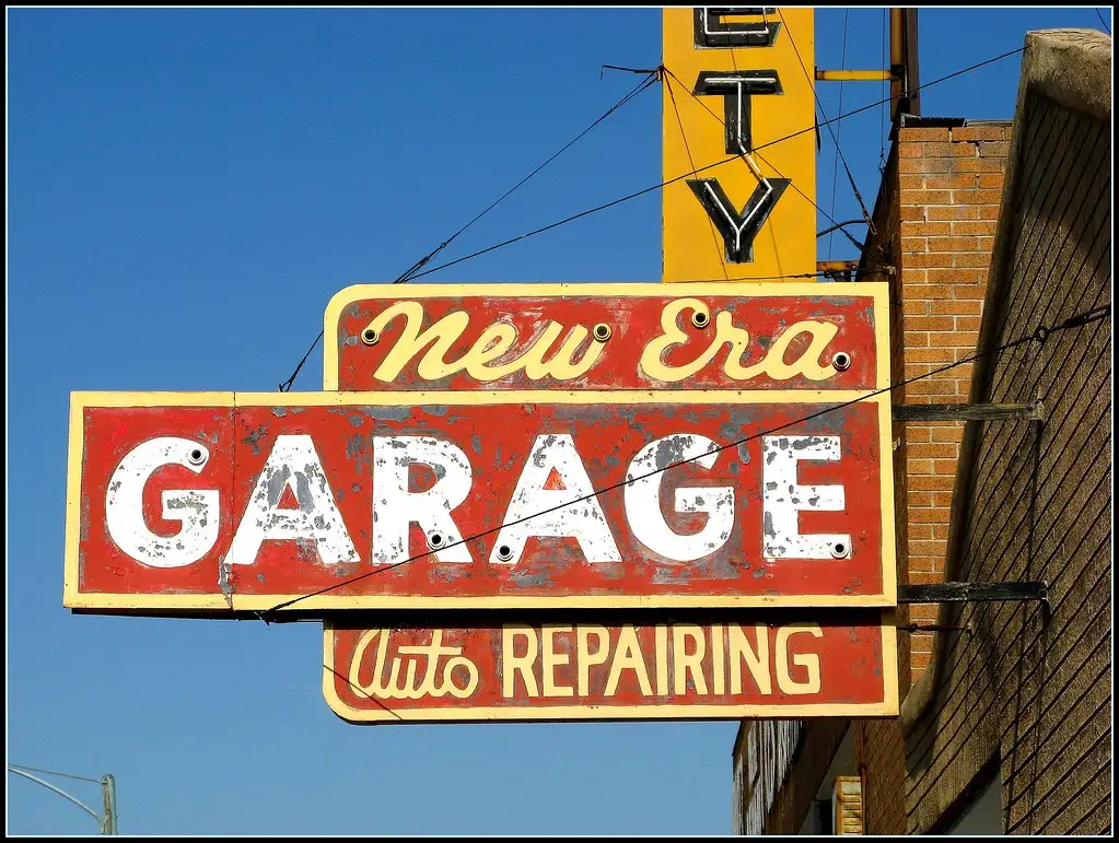 Car owner and mechanic reviewing service items beside a sedan at a neighborhood auto shop