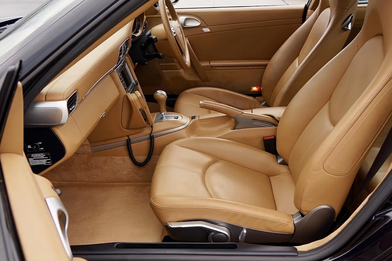 Detailer wiping a leather car seat and console with microfiber cloth in natural garage light