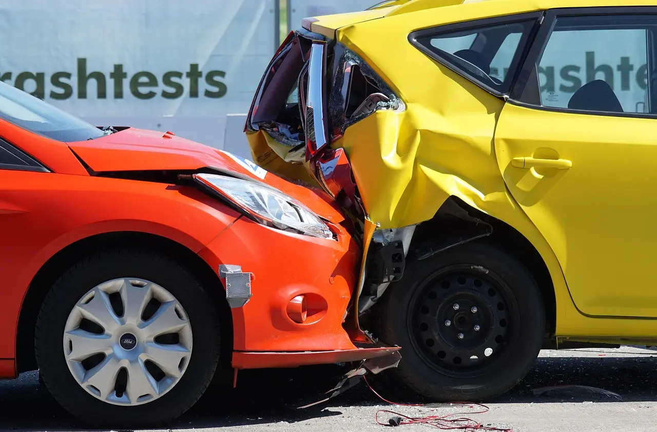 A driver reviews insurance paperwork beside a compact sedan in a sunny driveway.
