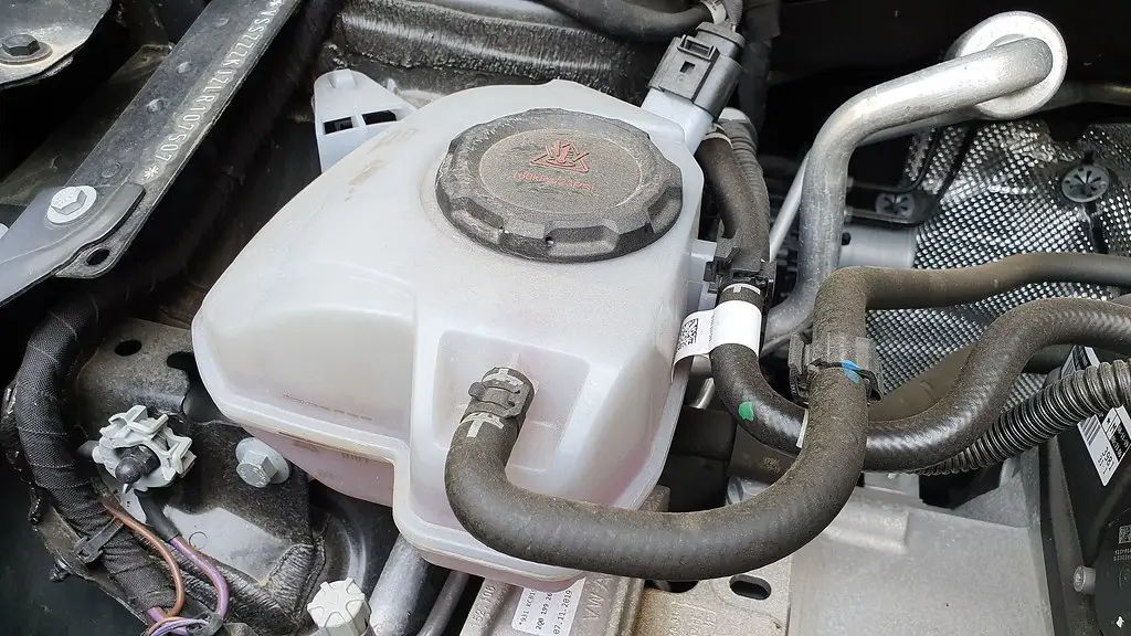 Gloved hand topping off coolant through a funnel into a reservoir