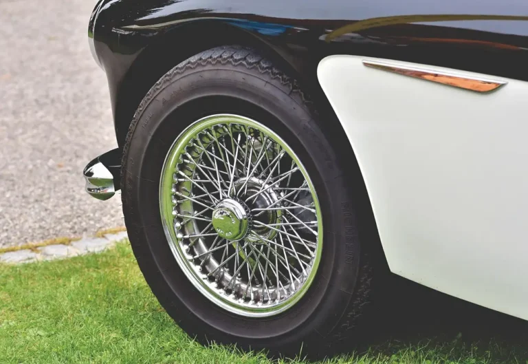 Classic car with custom wheels beside it while owner and mechanic compare fitment in natural light.