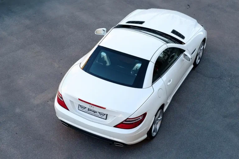 Detailer comparing spray bottles beside a wet dark sedan with microfiber towel