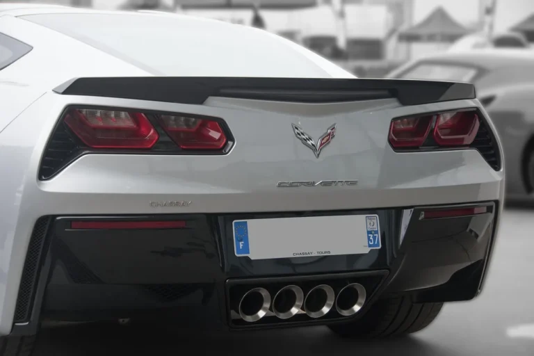 Mechanic inspecting a car's exhaust tip beside the rear bumper in natural light.