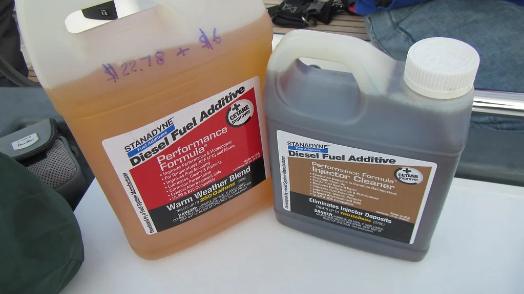 Gloved hands pour fuel stabilizer into a measuring cup beside a gas can