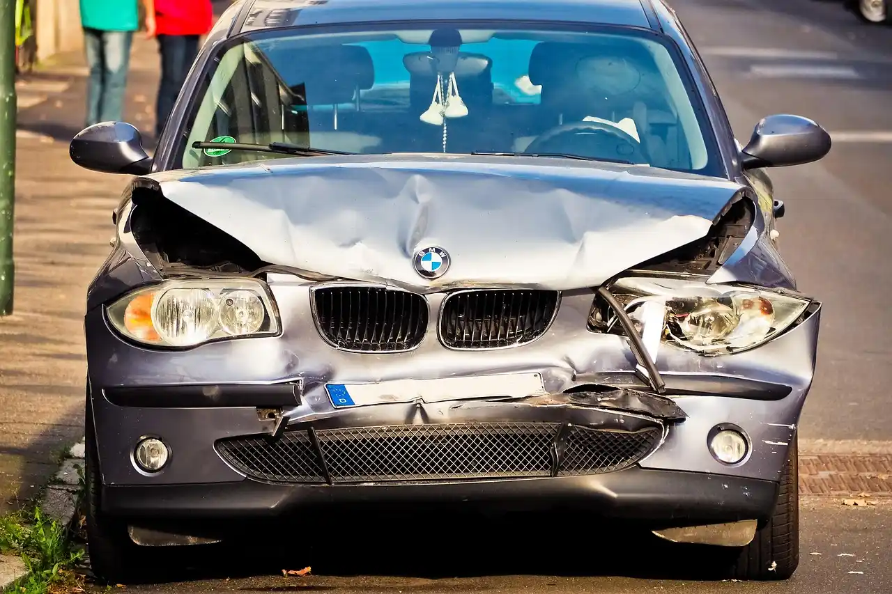 Person reviewing paperwork beside a damaged car in a sunny parking lot