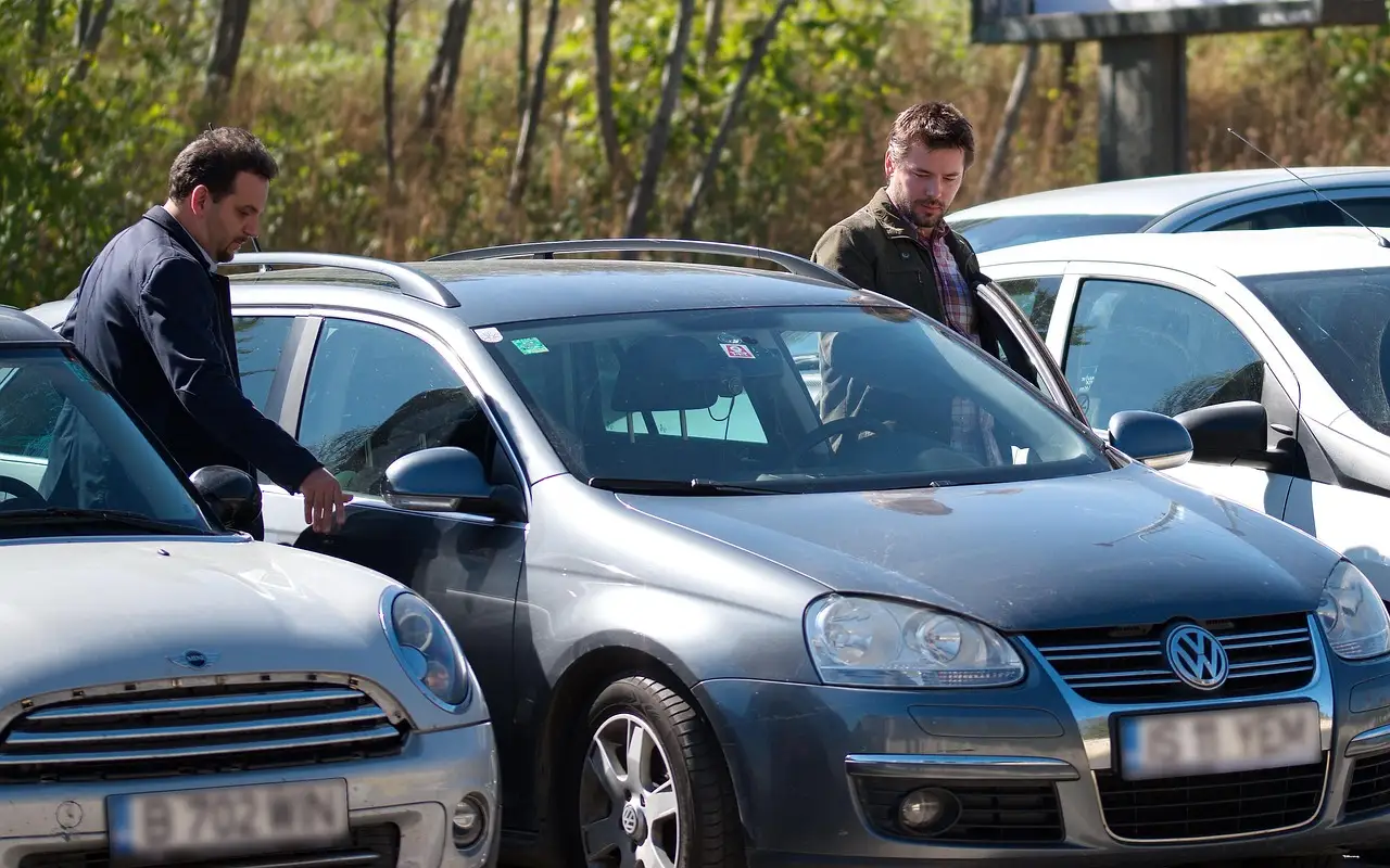 Car buyer and finance manager reviewing a loan quote at a dealership desk with a sedan outside