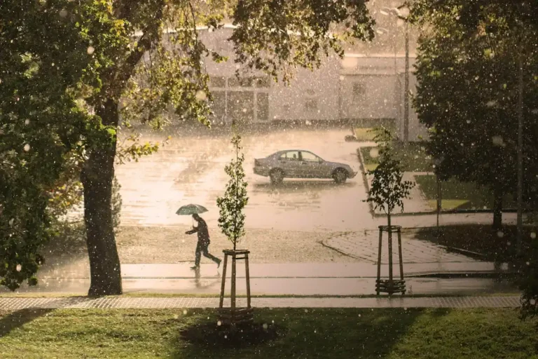 A person unfolding a hail protection cover beside a sedan in a driveway during a storm
