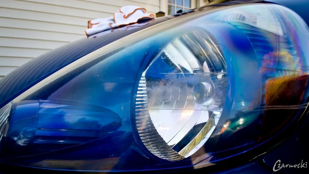 Hands sanding a yellowed headlight lens during headlight restoration
