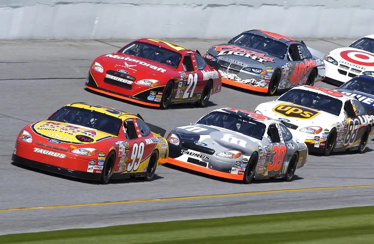 NASCAR stock car racing past the grandstands on an oval track at speed