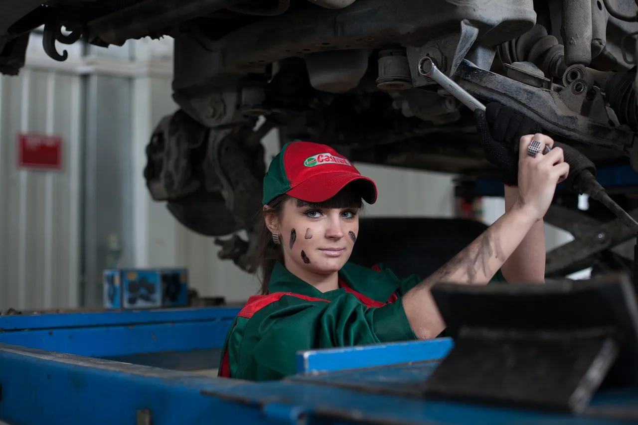 Mechanic and car owner beside a sedan in a service bay reviewing a maintenance checklist.