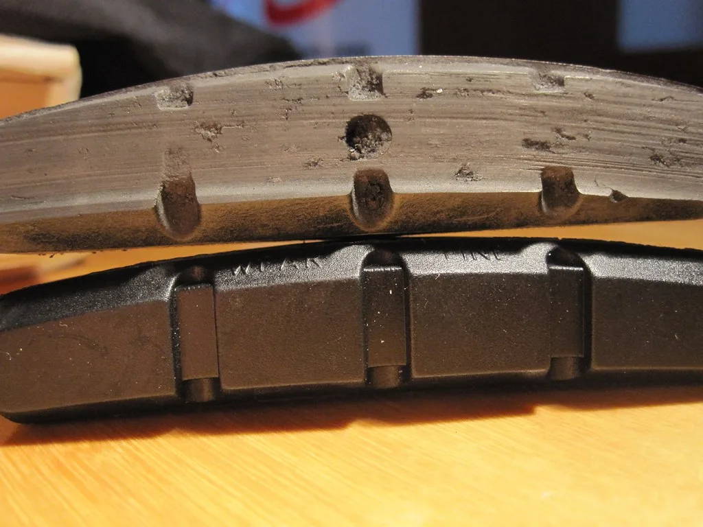 Worn brake pads and new pads beside a brake rotor on a garage bench