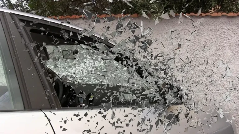 A person reviews auto insurance paperwork beside an older sedan with a calculator and clipboard