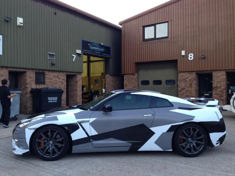 Race car being wrapped in a garage with vinyl panels and a technician at work