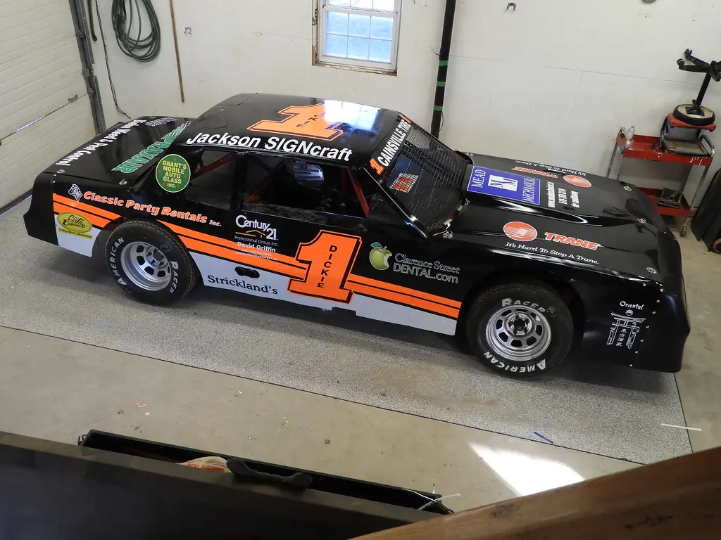 Hands trimming vinyl wrap on a race car panel with measuring tools nearby