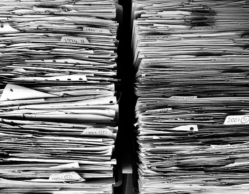 Buyer and mechanic reviewing service book, MOT papers, and invoices beside a used car