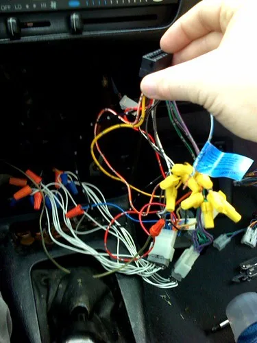 Hand holding a wire connector inside a car dashboard with exposed tangled wires