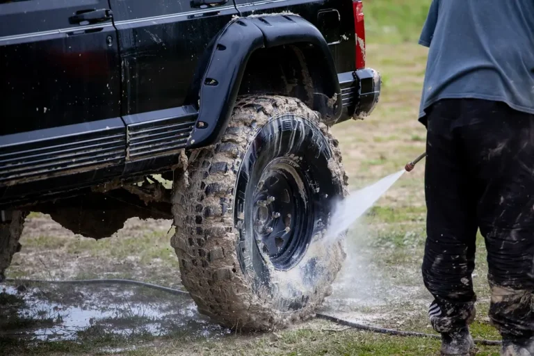 Muddy SUV at a trailhead with a hiker packing recovery gear and duffel bags