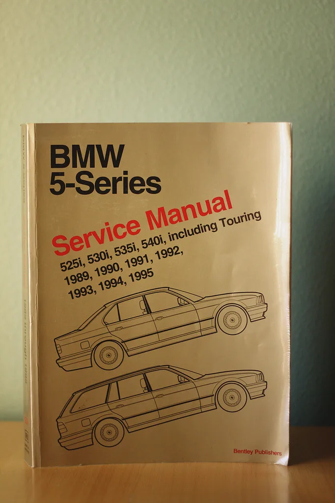 BMW sedan in a service bay with a mechanic checking an oil change list beside the open hood