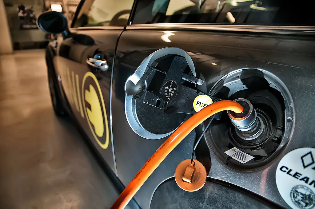 Hands attaching charger clamps to a car battery in a garage